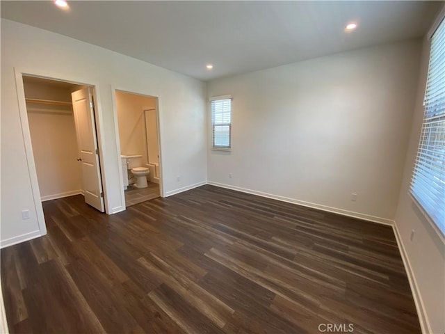 unfurnished bedroom featuring a spacious closet, dark wood-type flooring, and baseboards