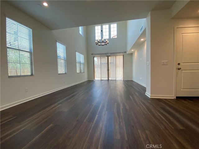 unfurnished living room with a high ceiling, baseboards, visible vents, dark wood-type flooring, and an inviting chandelier