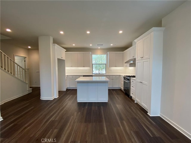 kitchen featuring a center island, gas range oven, under cabinet range hood, and dark wood-type flooring