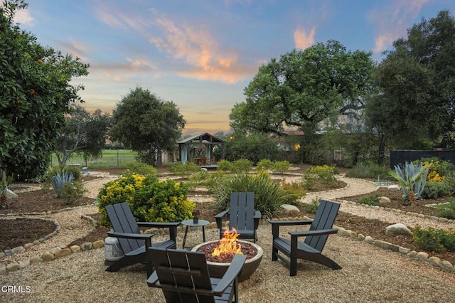 yard at dusk featuring fence, an outdoor fire pit, and a gazebo