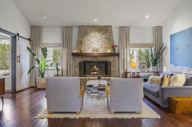 living area with a barn door, hardwood / wood-style floors, and a stone fireplace