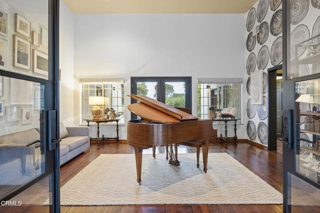 sitting room featuring hardwood / wood-style floors, baseboards, french doors, and a towering ceiling