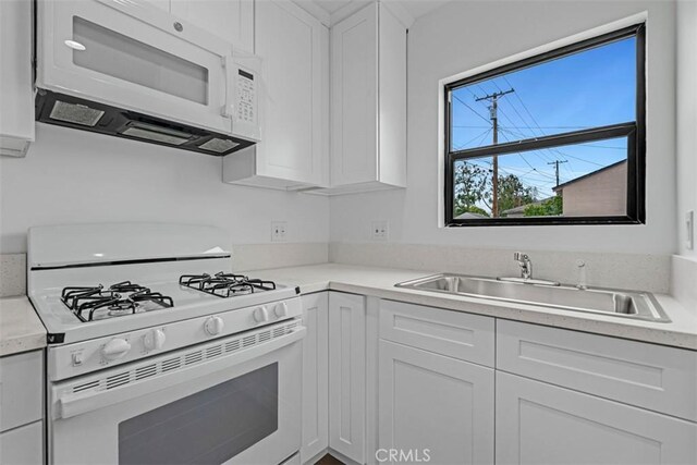 kitchen with a sink, white cabinets, white appliances, and light countertops