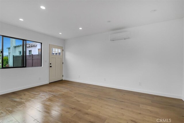 empty room featuring plenty of natural light, a wall mounted AC, and wood finished floors