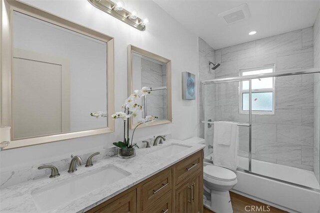 bathroom with double vanity, a sink, combined bath / shower with glass door, and toilet