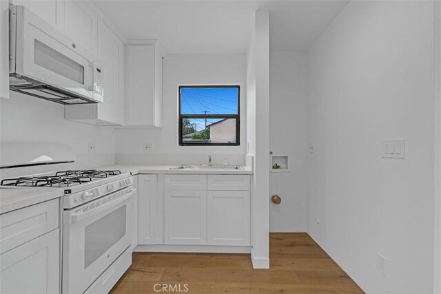 kitchen with a sink, light countertops, white appliances, and white cabinetry