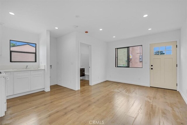 interior space with light wood-type flooring, recessed lighting, a sink, and baseboards
