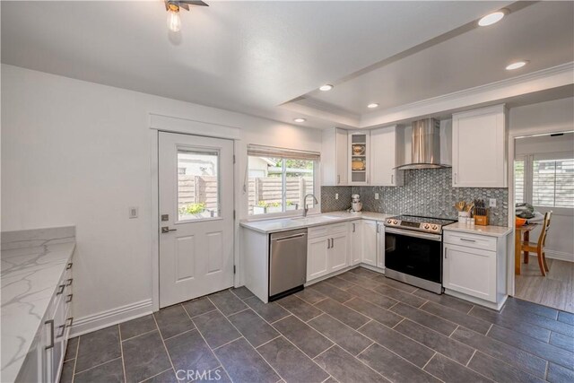 kitchen with backsplash, a raised ceiling, a sink, wall chimney range hood, and appliances with stainless steel finishes
