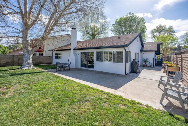 rear view of property with a chimney, a fenced backyard, stucco siding, a yard, and a patio area