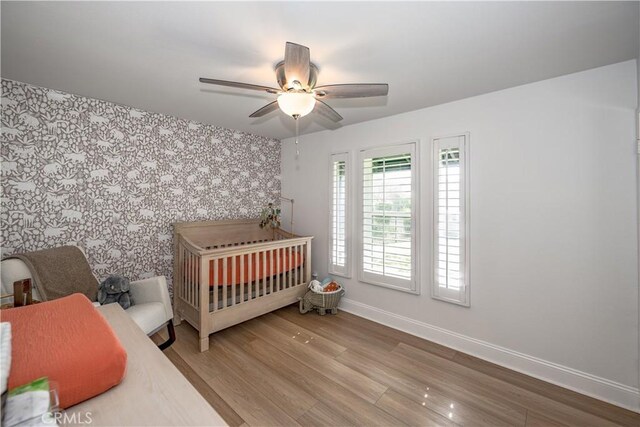bedroom with a nursery area, an accent wall, wood finished floors, baseboards, and wallpapered walls