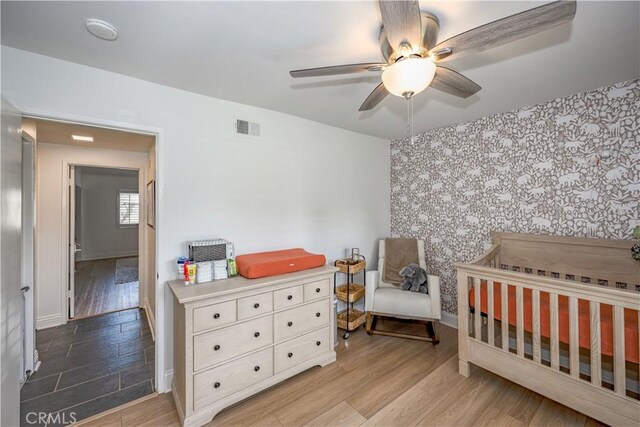 bedroom with an accent wall, visible vents, light wood-style flooring, and a nursery area
