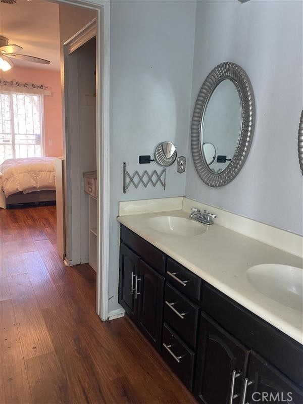 ensuite bathroom with double vanity, a sink, ceiling fan, and wood finished floors