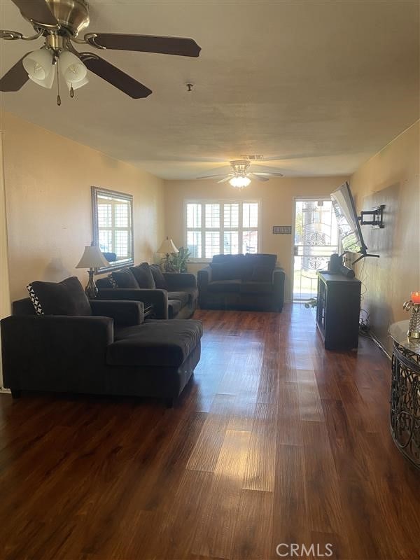 living area with a healthy amount of sunlight, dark wood-style flooring, and a ceiling fan