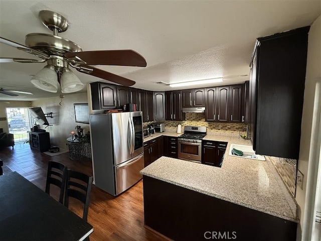 kitchen featuring tasteful backsplash, stainless steel appliances, under cabinet range hood, a ceiling fan, and a peninsula