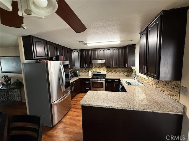 kitchen featuring stainless steel appliances, under cabinet range hood, a sink, visible vents, and light wood-style flooring