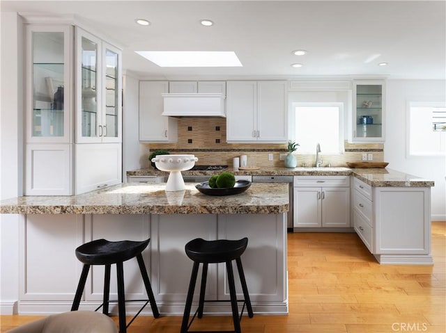 kitchen featuring a sink, a skylight, a peninsula, stainless steel dishwasher, and light wood-style floors