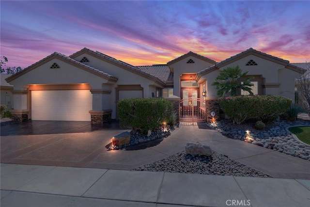 mediterranean / spanish house with a gate, concrete driveway, stucco siding, an attached garage, and a tiled roof