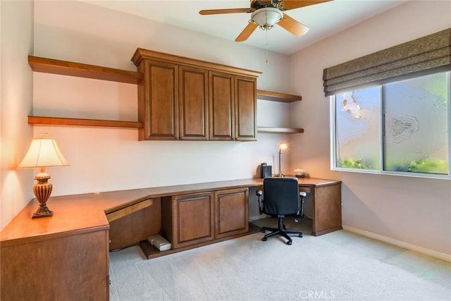 home office with baseboards, built in desk, ceiling fan, and light carpet