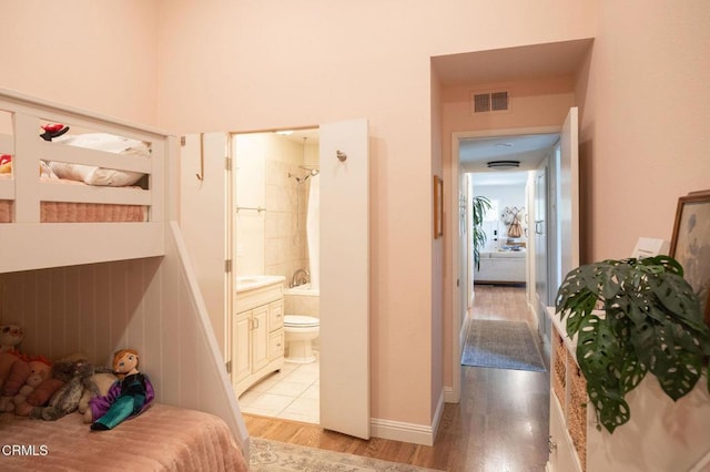 bedroom with baseboards, ensuite bath, light wood-style floors, and visible vents