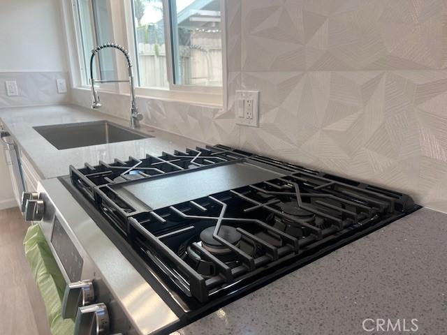 1197 Colony Dr, Pomona, CA 91766 - interior details featuring a sink, cooktop, decorative backsplash, and light stone counters