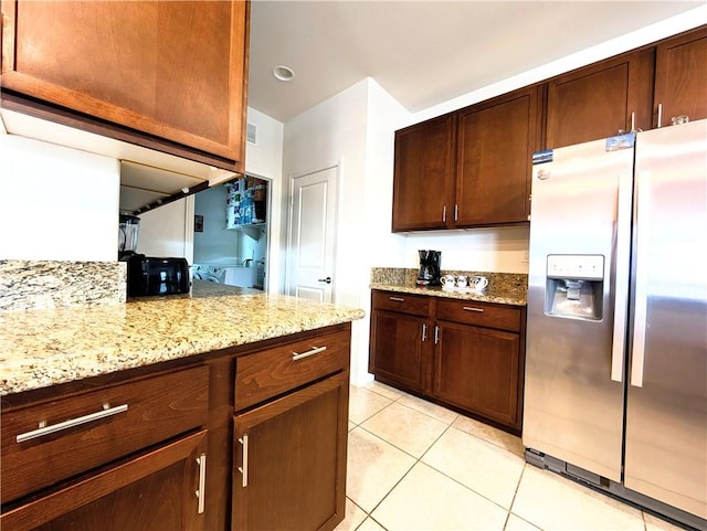 kitchen featuring light stone countertops, stainless steel refrigerator with ice dispenser, visible vents, and light tile patterned floors