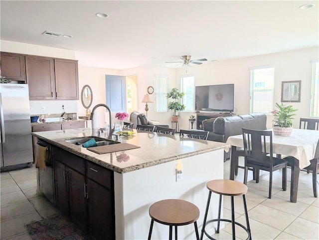 kitchen with freestanding refrigerator, light tile patterned floors, a kitchen bar, a sink, and visible vents