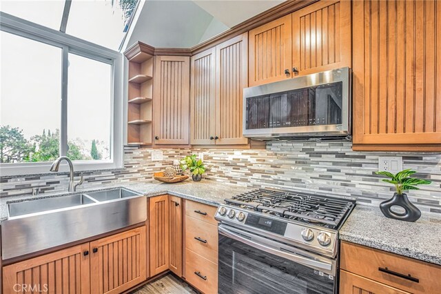 kitchen with open shelves, tasteful backsplash, light stone counters, a sink, and appliances with stainless steel finishes