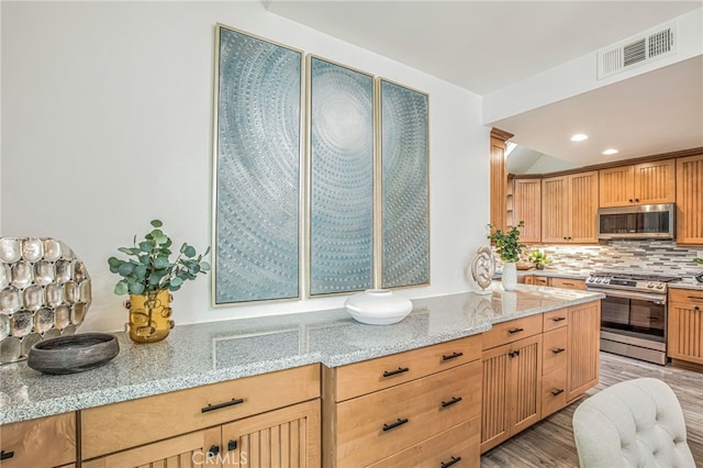 kitchen featuring appliances with stainless steel finishes, light stone counters, light wood-style flooring, backsplash, and visible vents