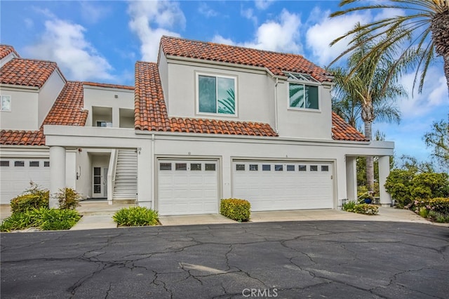 view of front of house with a tiled roof, an attached garage, stucco siding, and aphalt driveway