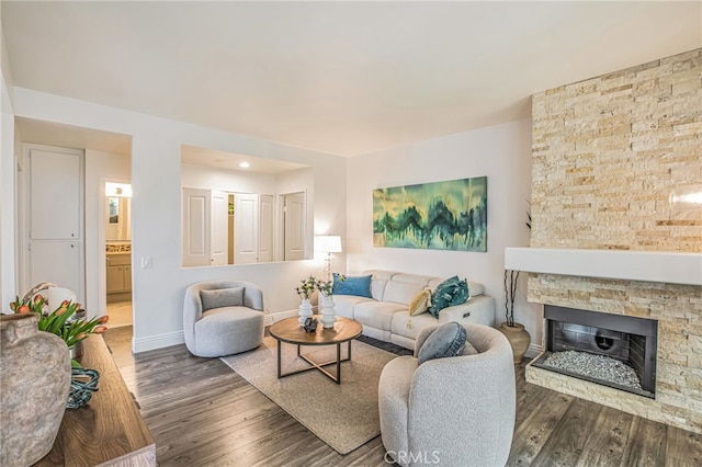 living room with baseboards, a stone fireplace, and wood finished floors