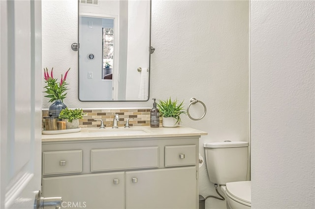 bathroom featuring toilet, visible vents, decorative backsplash, and vanity