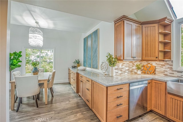 kitchen with stainless steel dishwasher, lofted ceiling, light stone countertops, backsplash, and a notable chandelier