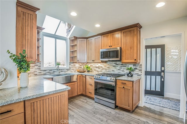 kitchen with appliances with stainless steel finishes, tasteful backsplash, open shelves, a sink, and light wood finished floors