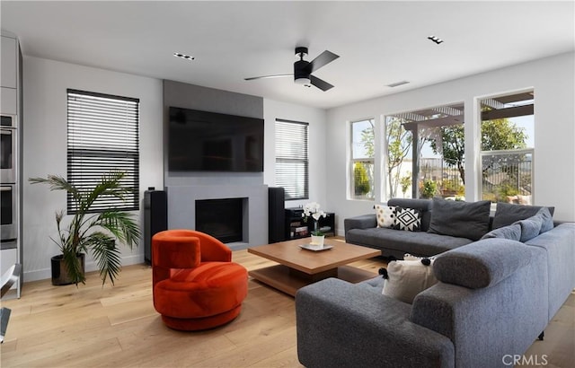 living room with visible vents, a fireplace, light wood-style floors, and ceiling fan