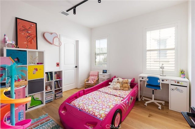 bedroom featuring rail lighting, wood finished floors, and visible vents