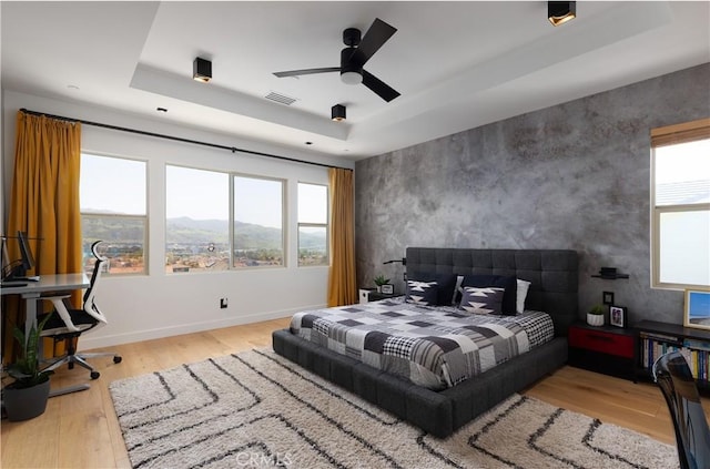 bedroom featuring multiple windows, wood finished floors, a tray ceiling, and a mountain view
