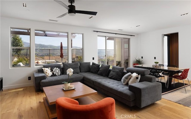 living room with baseboards, light wood-style flooring, visible vents, and a ceiling fan