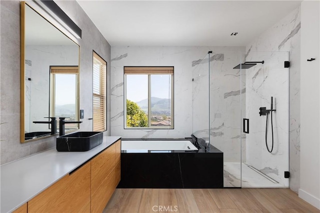full bathroom featuring a bath, vanity, wood finished floors, and a marble finish shower