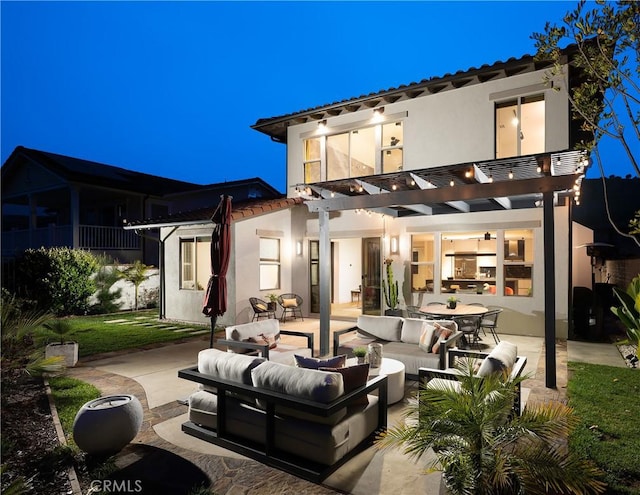 back of house at night with stucco siding, outdoor lounge area, a patio, and a pergola