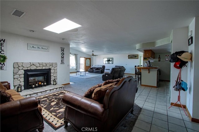 7469 Madera Ave, Hesperia, CA 92345 - tiled living room with a stone fireplace, visible vents, a ceiling fan, baseboards, and vaulted ceiling with skylight