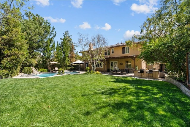 rear view of property with stucco siding, a patio, an outdoor pool, a lawn, and a chimney
