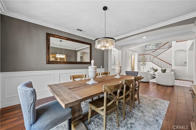dining area with dark wood-style flooring, a chandelier, stairs, ornamental molding, and wainscoting
