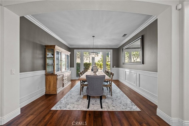dining room featuring dark wood finished floors, ornamental molding, and a wainscoted wall