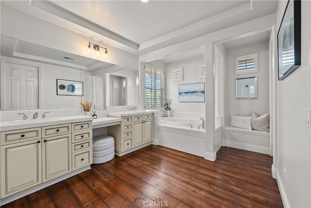 bathroom featuring a raised ceiling, hardwood / wood-style floors, a garden tub, vanity, and baseboards