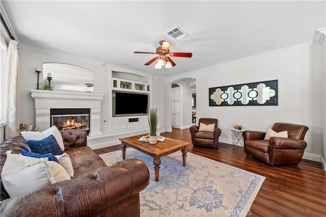 living area featuring arched walkways, a glass covered fireplace, wood finished floors, ceiling fan, and ornamental molding
