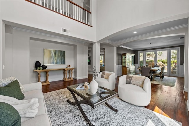 living area featuring crown molding, wood finished floors, baseboards, a towering ceiling, and arched walkways
