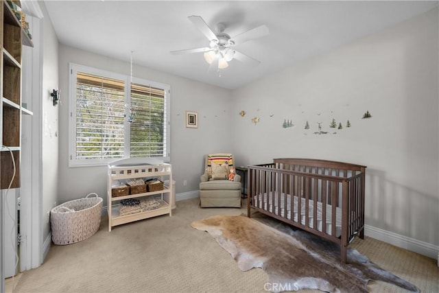 carpeted bedroom featuring baseboards, a crib, and a ceiling fan