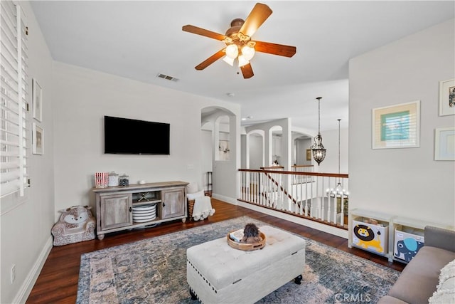 living area with wood finished floors, arched walkways, a ceiling fan, and baseboards