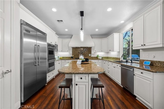 kitchen with built in appliances, a sink, a breakfast bar area, white cabinetry, and recessed lighting