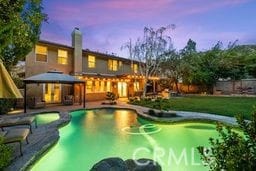 pool at dusk with a gazebo, a pool with connected hot tub, and a yard